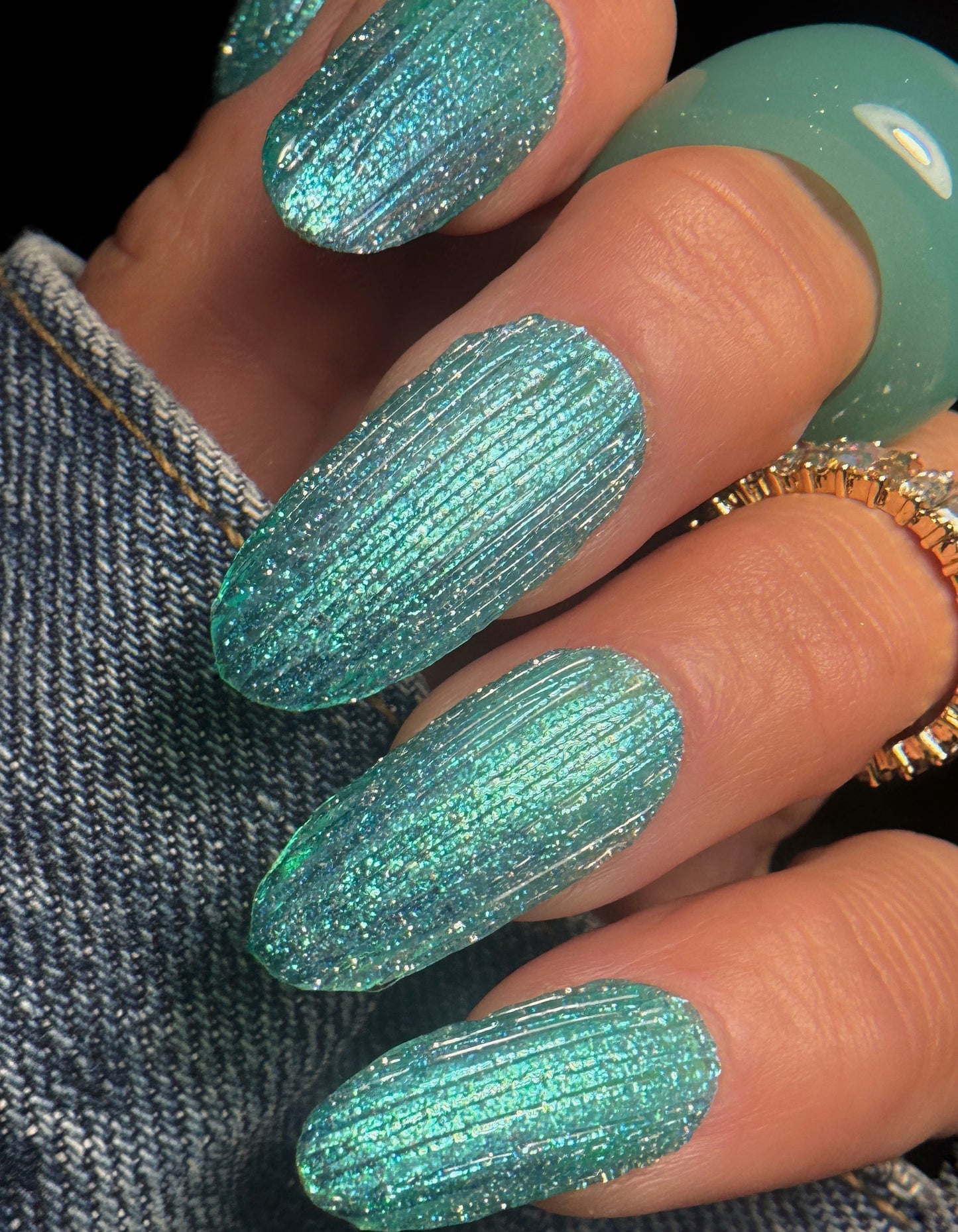 Close-up of a hand with teal glittery textured nail art on a dark background