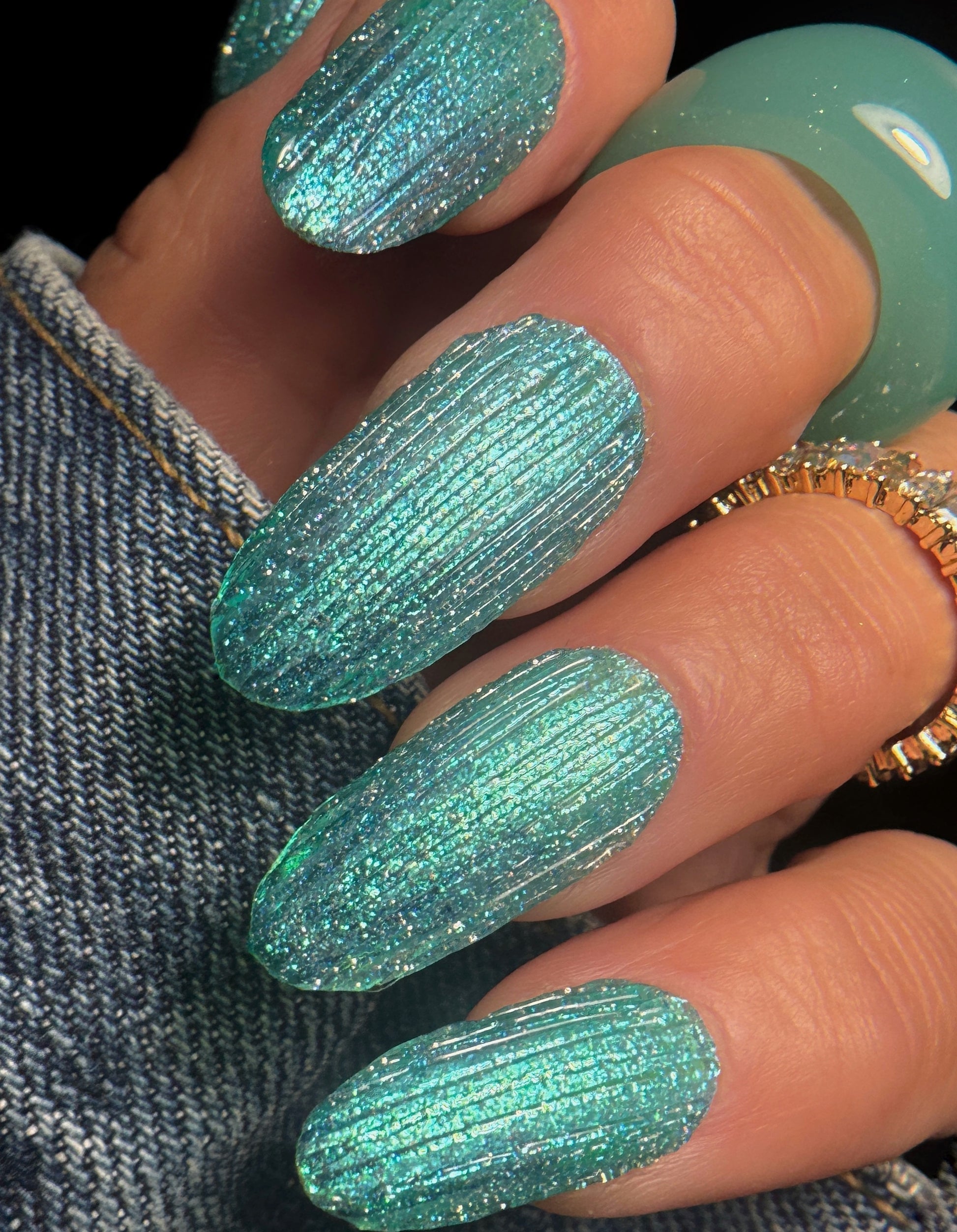 Close-up of a hand with teal glittery textured nail art on a dark background