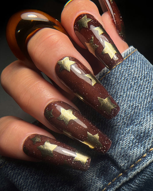 Nails with brown and gold star design on denim background