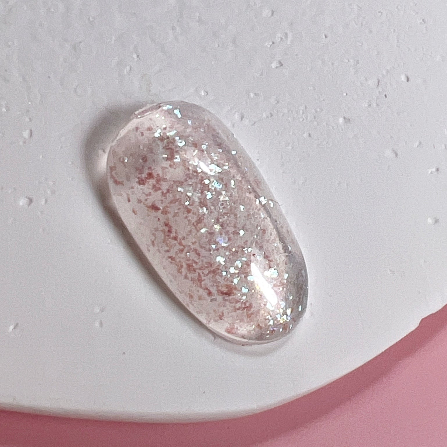 Decorated nail tip on textured white surface and pink background.