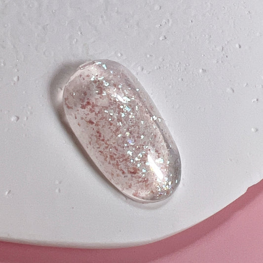 Decorated nail tip on textured white surface and pink background.