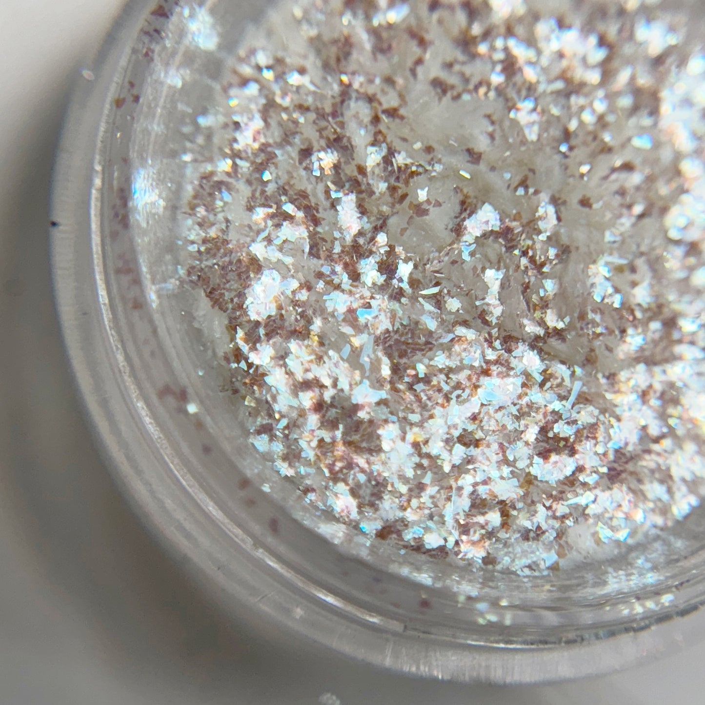 Close up of iridescent flakes in transparent jar on blurred background.