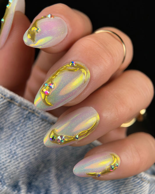 Nails with a gold and iridescent design held by a person wearing a denim jacket.
