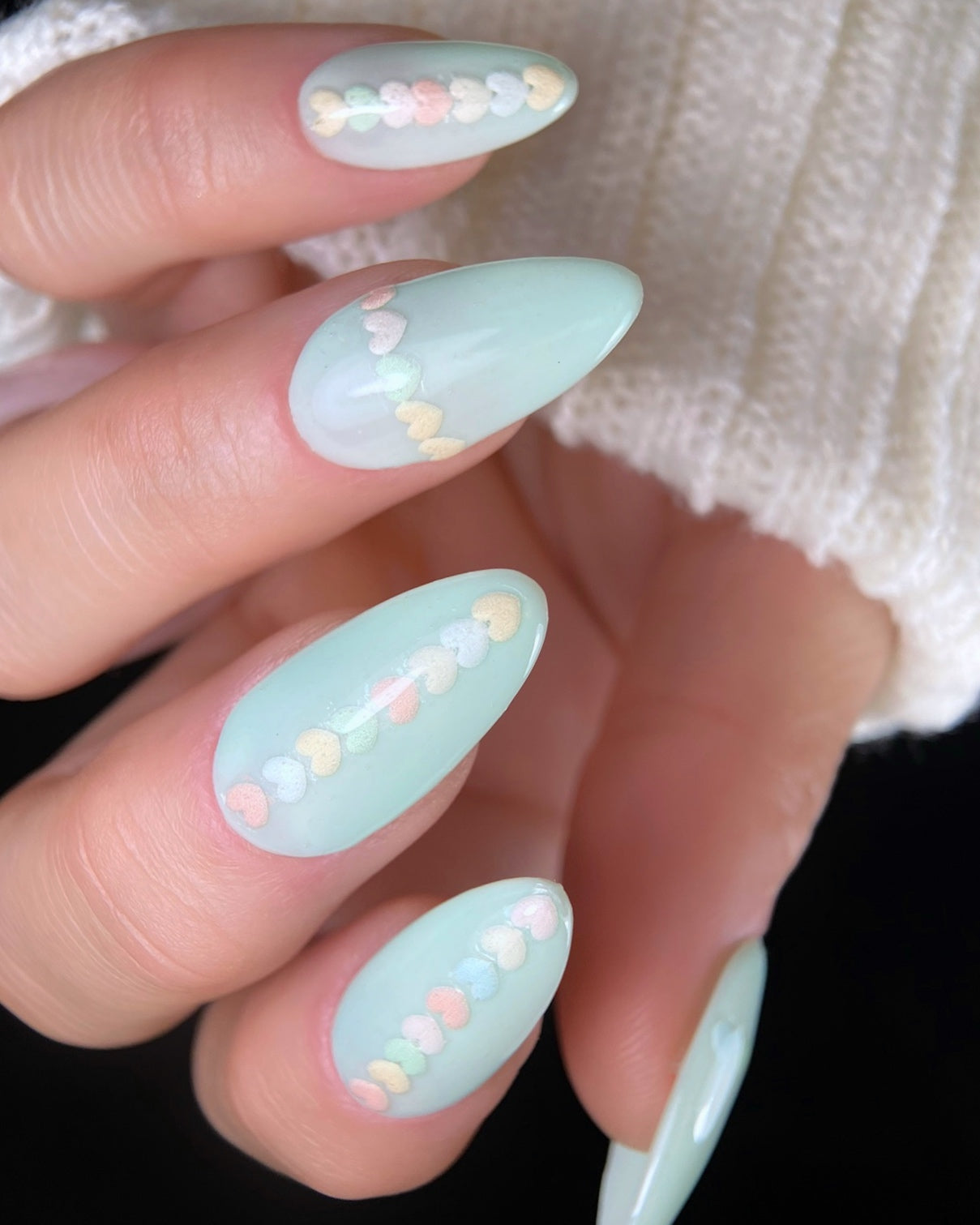 Mint green nails with heart-shaped decorations on a blurred background