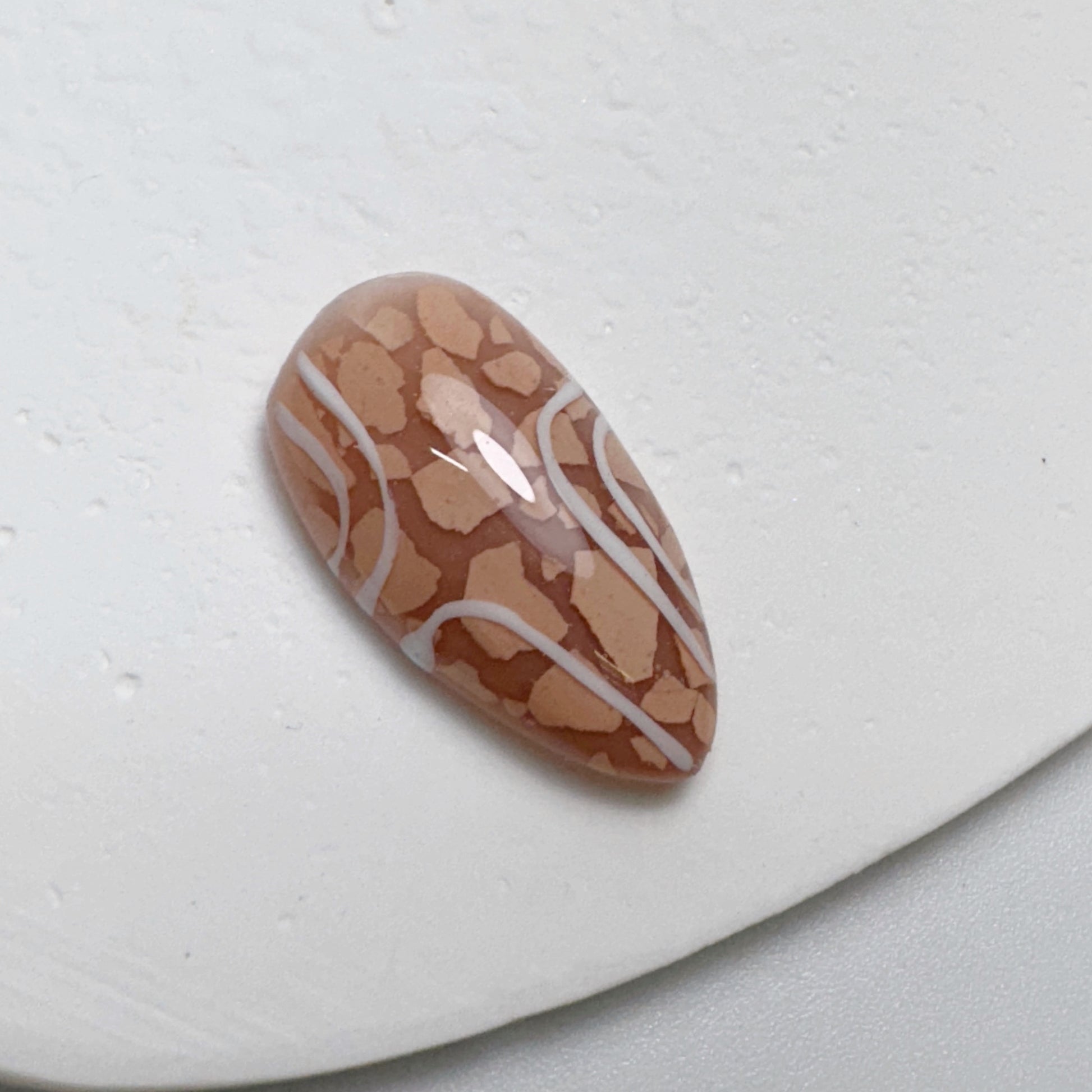 Decorated nail tip on white textured surface.