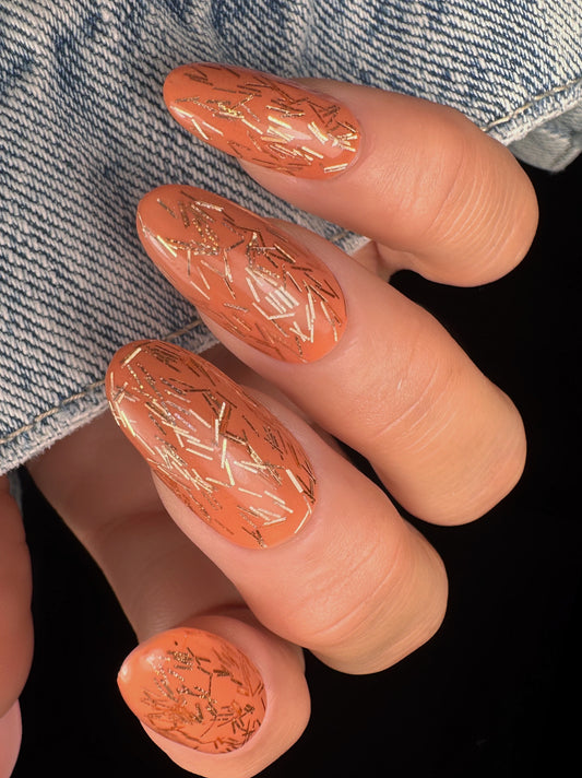 Nails with a decorative peach glitter pattern on a denim background