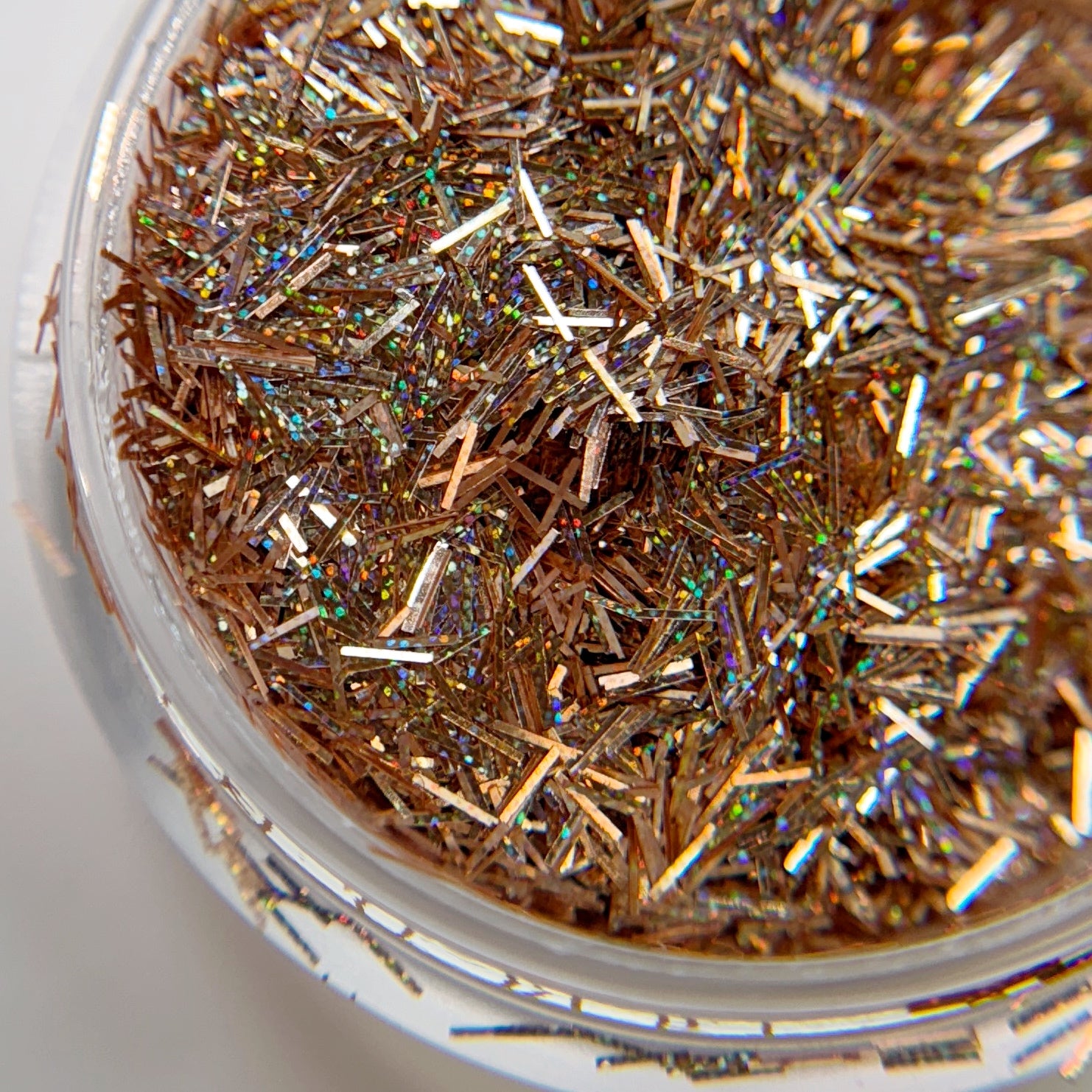 A close-up image of peach-colored tinsel glitter contained within a clear jar, showcasing its shiny and reflective surface.