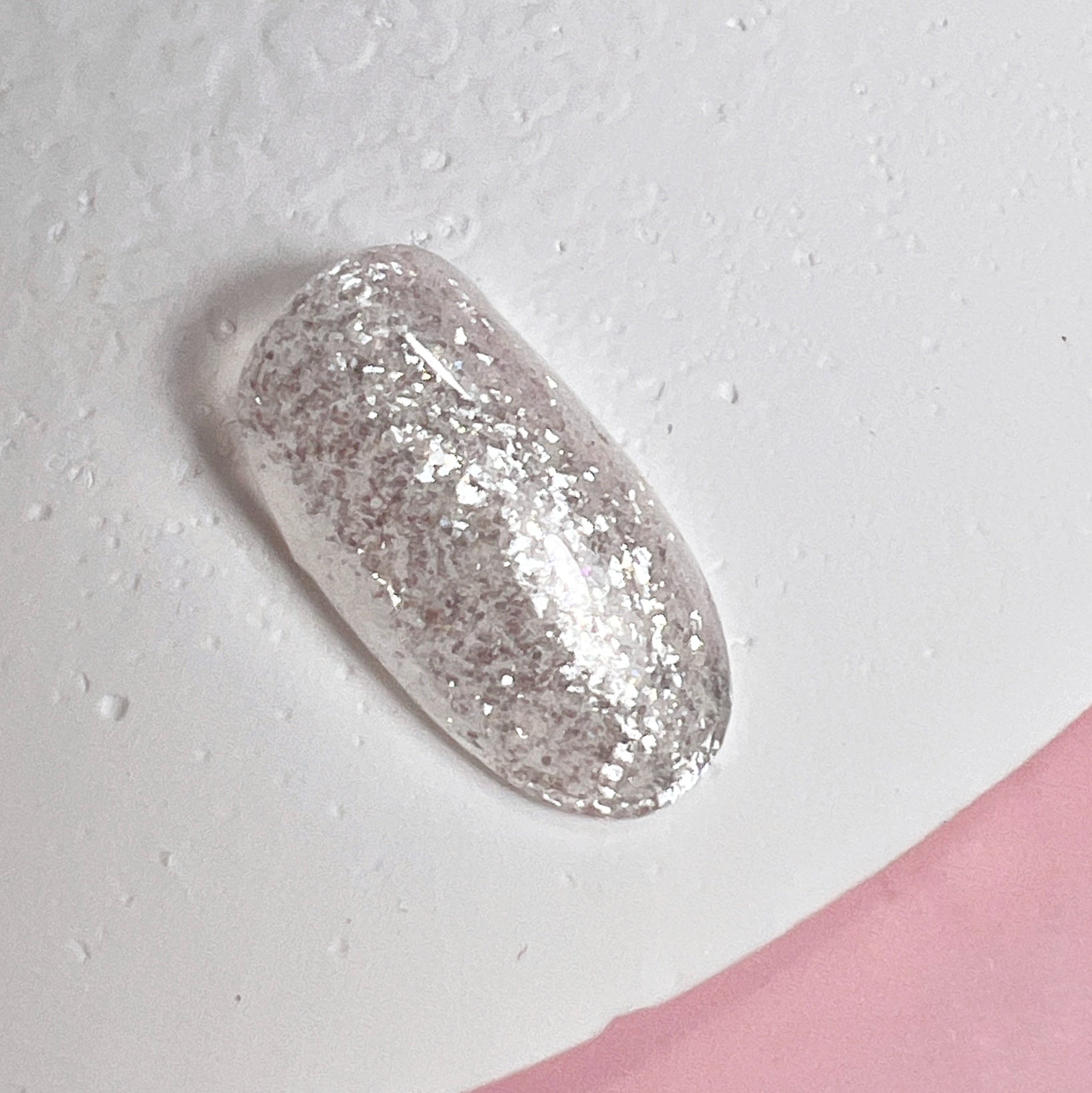 Decorated nail tip on textured white surface and pink background.