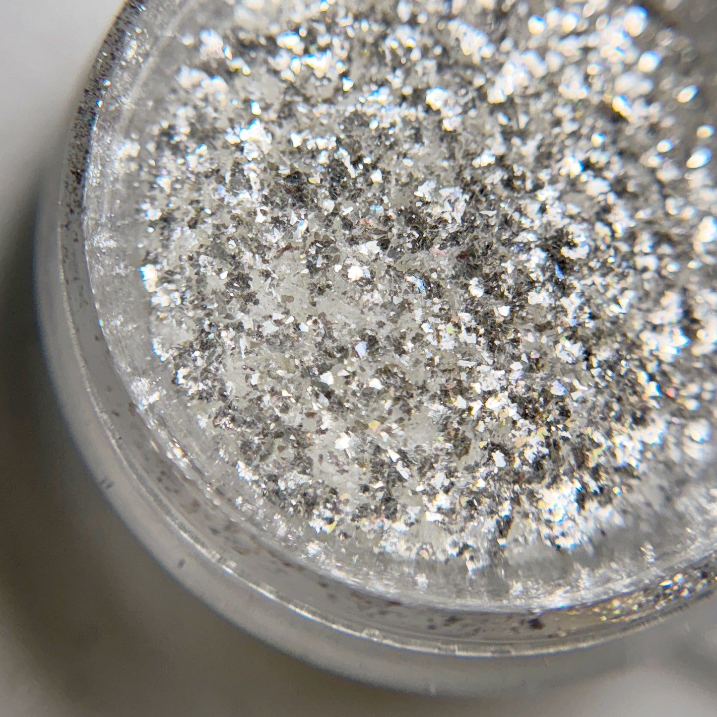 Close up of iridescent flakes in transparent jar on blurred background.