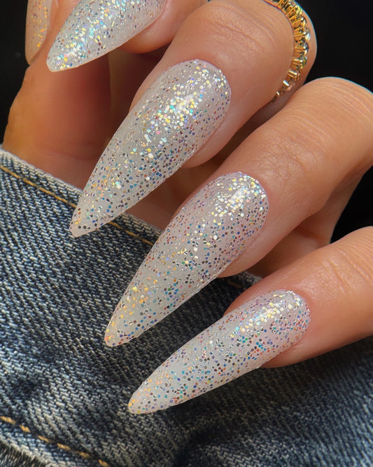 Close-up of a hand with glittery, stiletto nails on a denim background