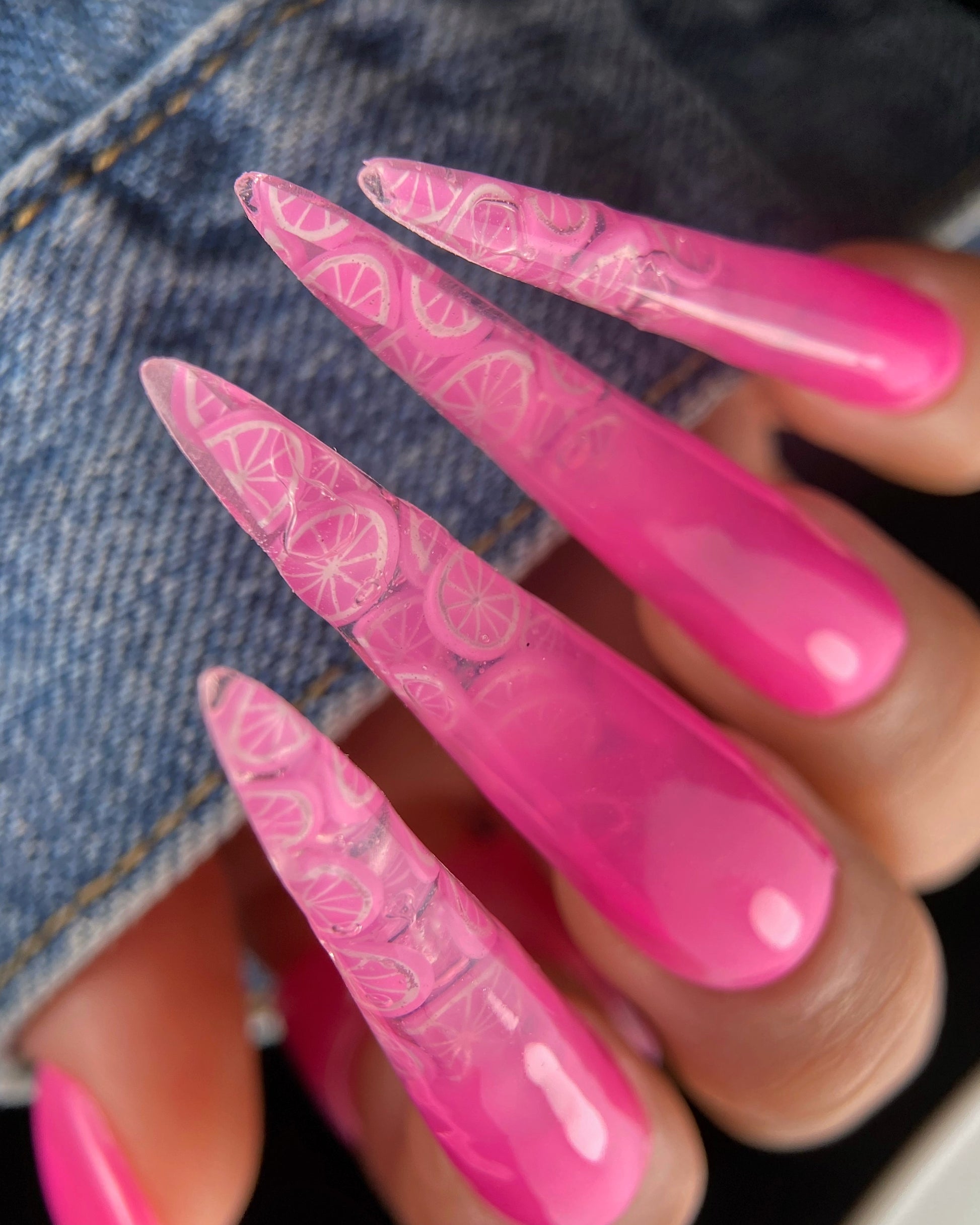 Close-up of a hand with pink nail polish and lace design on a denim background