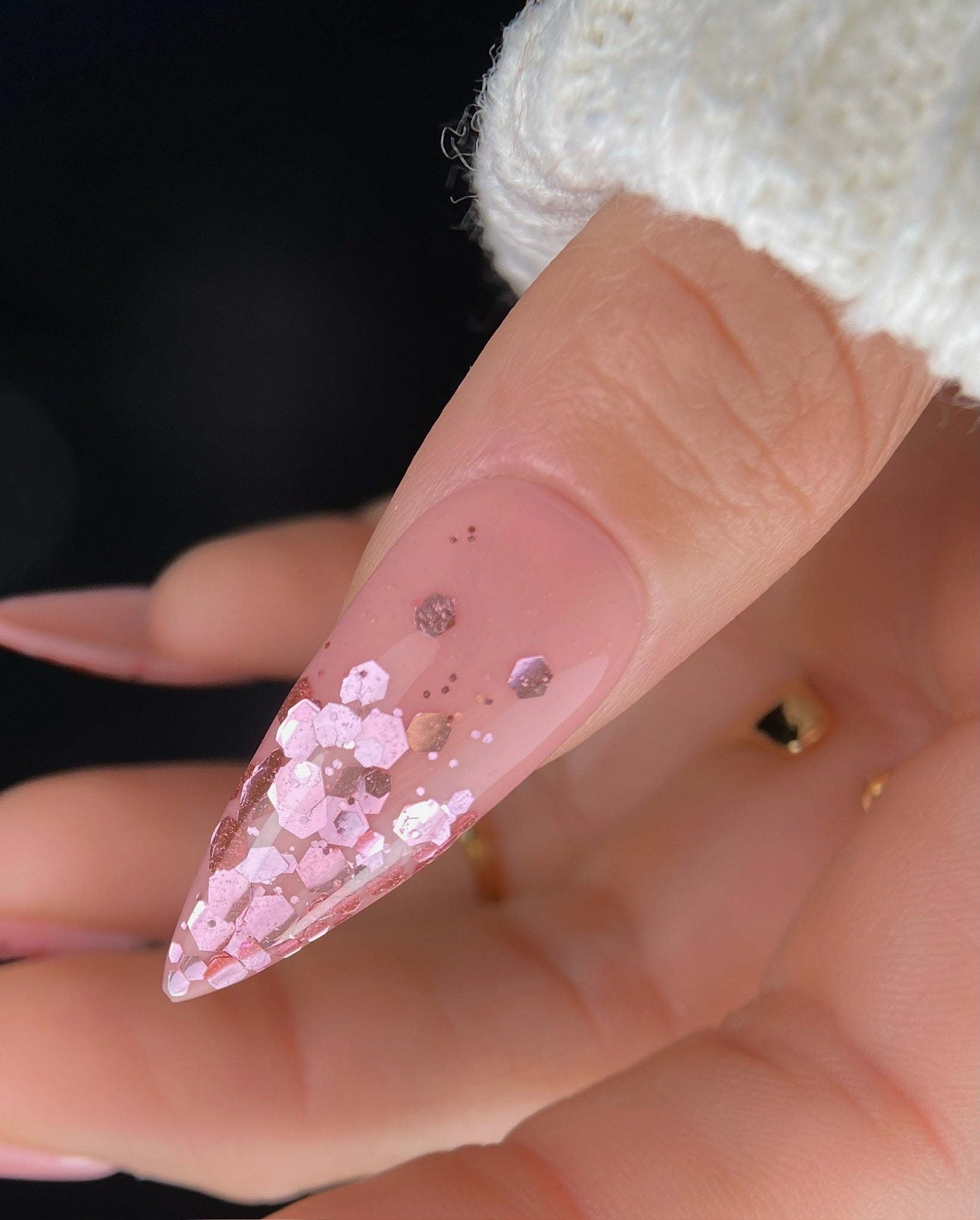 Close-up of a hand with a pink stiletto nail featuring glitter.