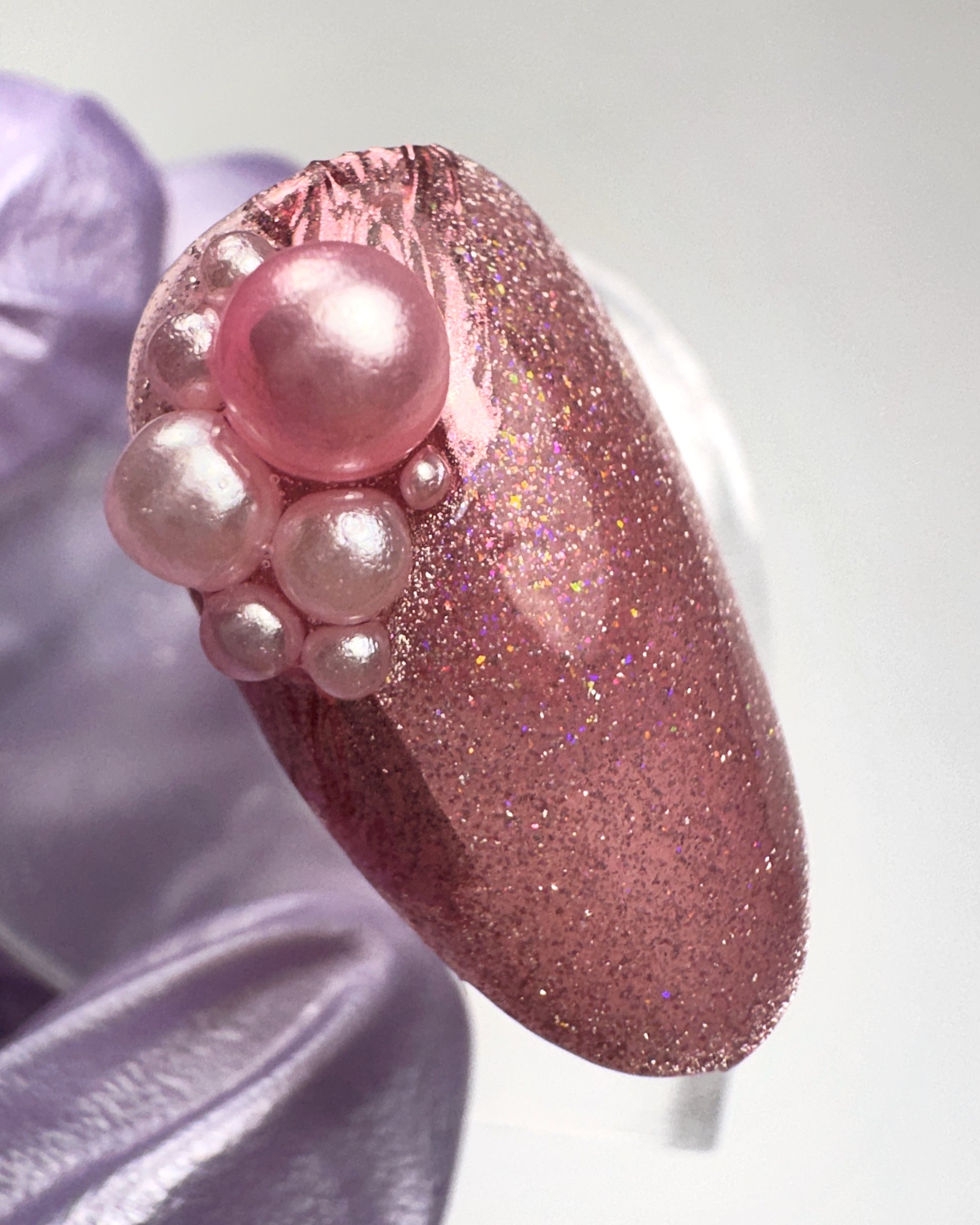 Pink glittery nail with pearl-like decorations on a light background