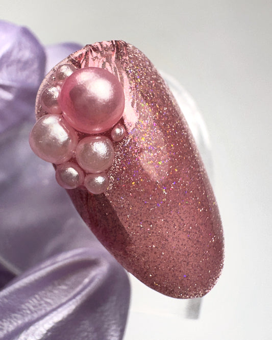 Pink glittery nail with pearl-like decorations on a light background