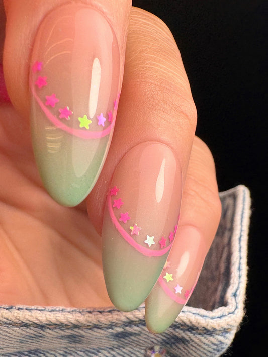 Nail art with green gradient nail art and pink star glitter designs on a black background