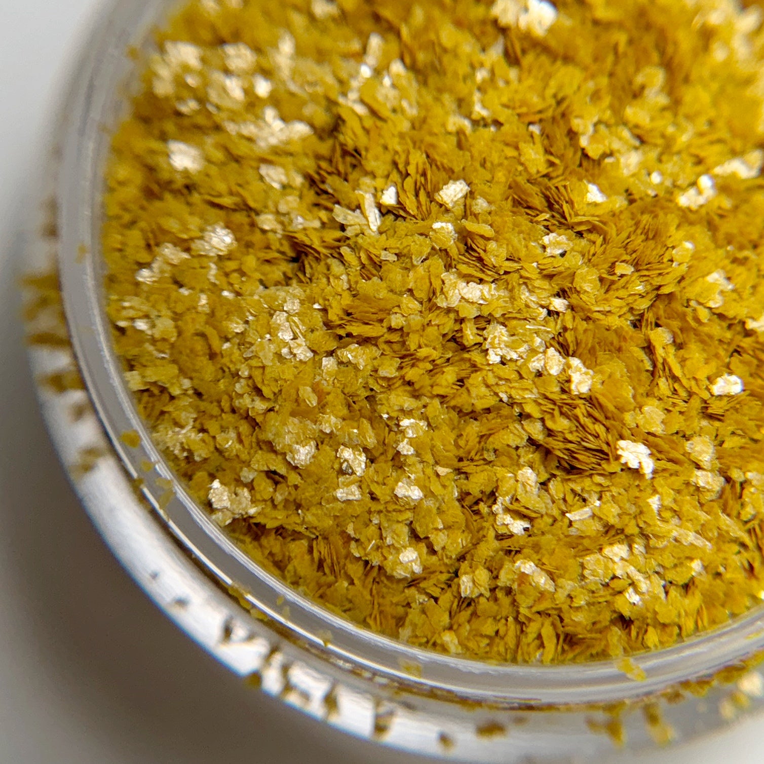 Close-up of a container filled with yellow flaky glitter on a white background