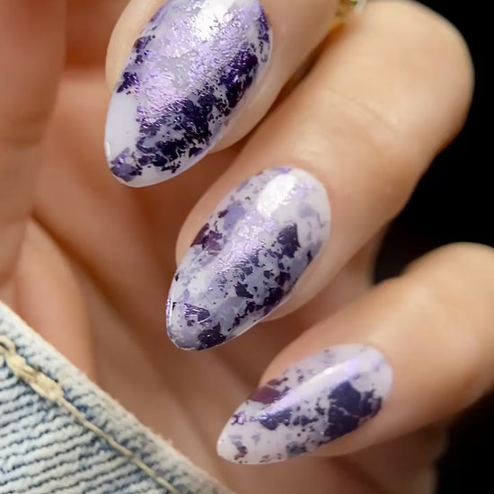 Close-up video of almond-shaped nails with Vacation Nail Shop Plum Foil Flakies over a sheer milky lavender base, showing the purple metallic reflection as the nails move.