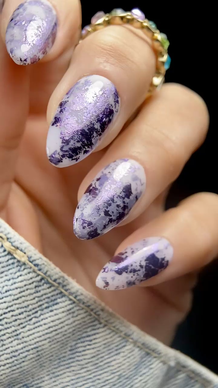 Close-up video of almond-shaped nails with Vacation Nail Shop Plum Foil Flakies over a sheer milky lavender base, showing the purple metallic reflection as the nails move.