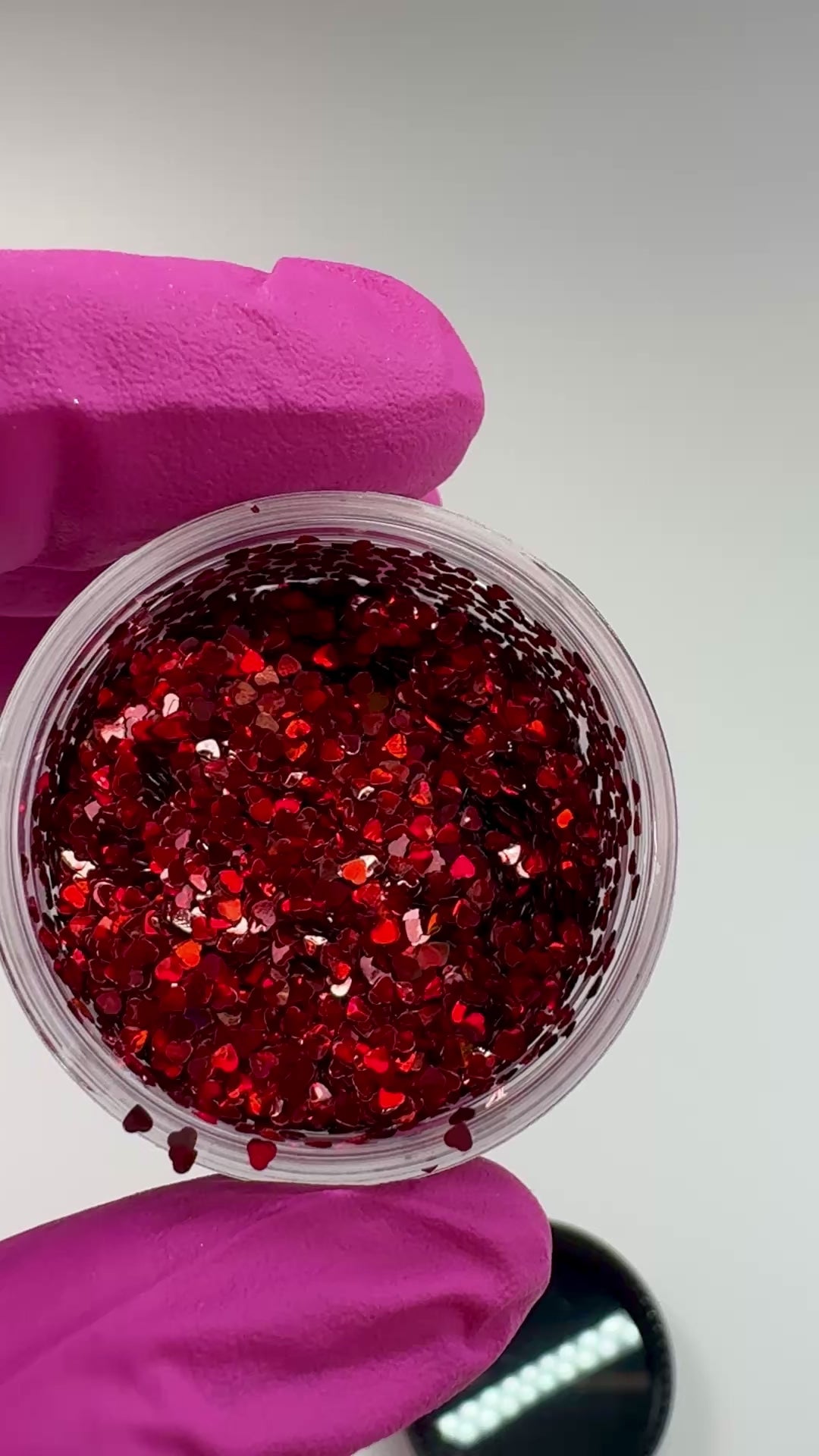 Video of gloved hand holding clear jar with textured glitter. 