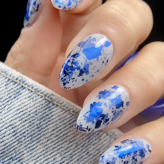 Close-up video of almond-shaped nails with Vacation Nail Shop Navy Foil Flakies over a sheer milky gray base, showing the bright blue metallic reflection as the nails move.