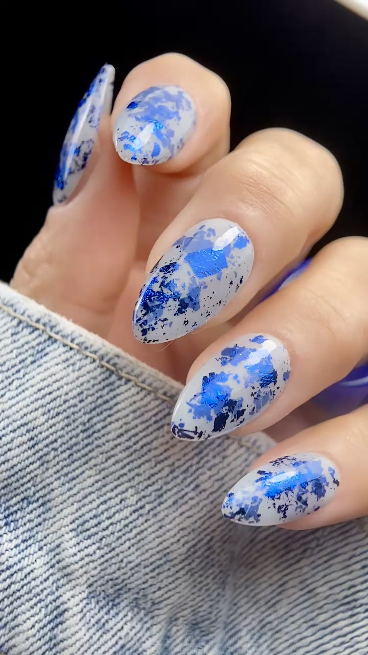 Close-up video of almond-shaped nails with Vacation Nail Shop Navy Foil Flakies over a sheer milky gray base, showing the bright blue metallic reflection as the nails move.