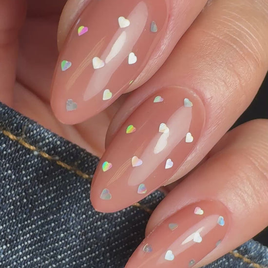 Video of hand in denim sleeve with silver nail art on neutral background.