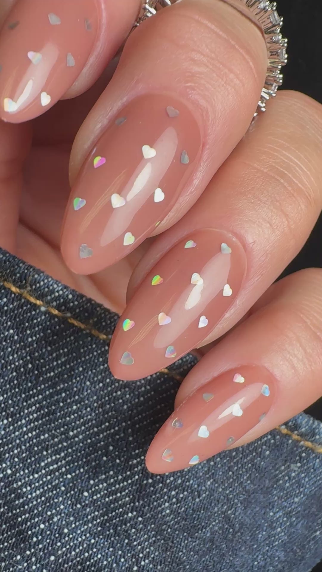 Video of hand in denim sleeve with silver nail art on neutral background.