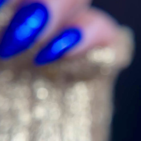 Video of manicured hand with blue glitter nail design on dark background