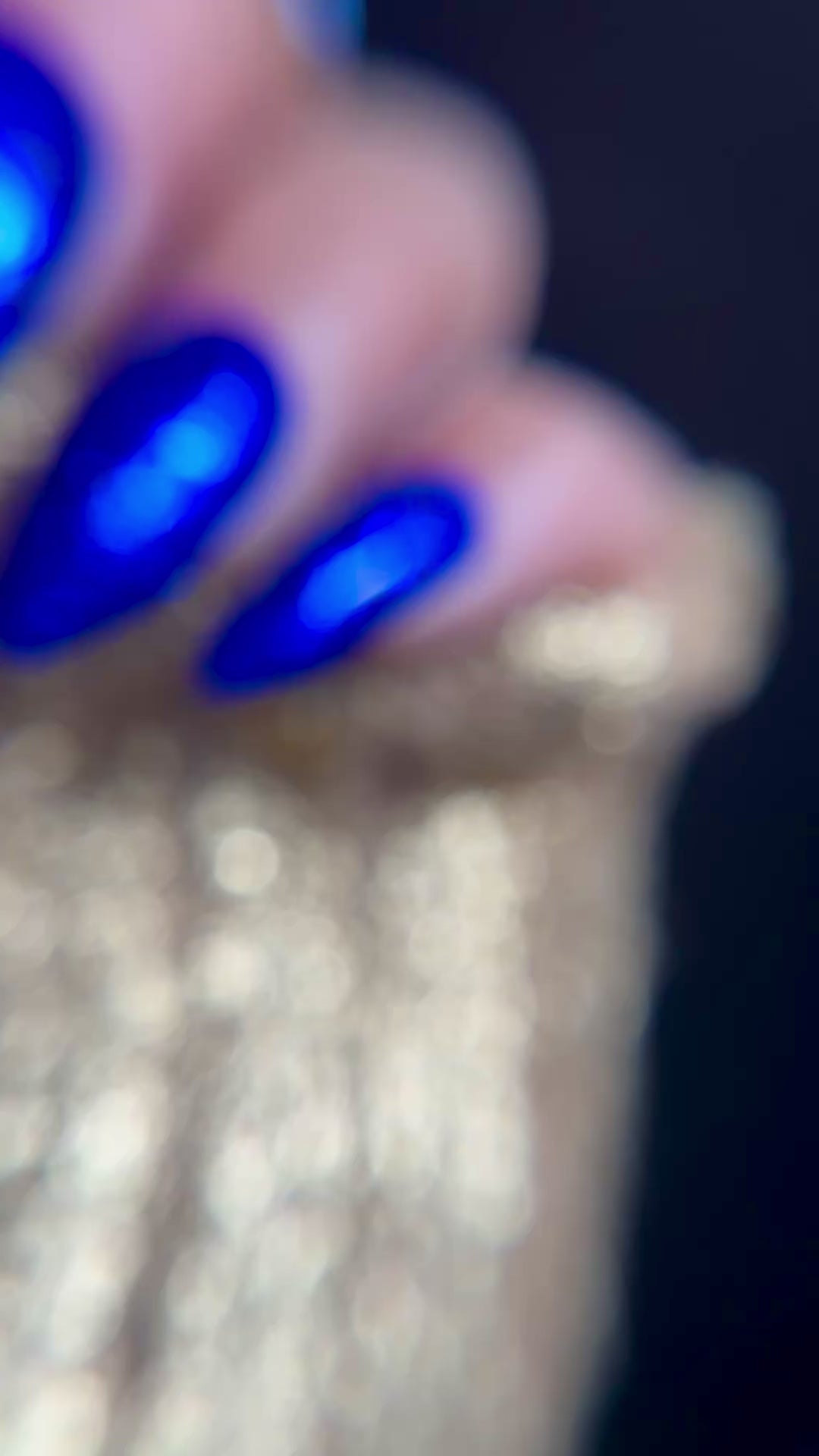 Video of manicured hand with blue glitter nail design on dark background