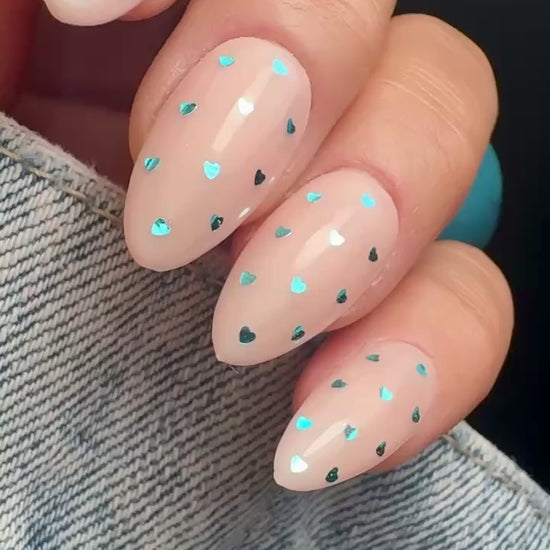 Video of nails with blue heart shaped glitter design on neutral background.