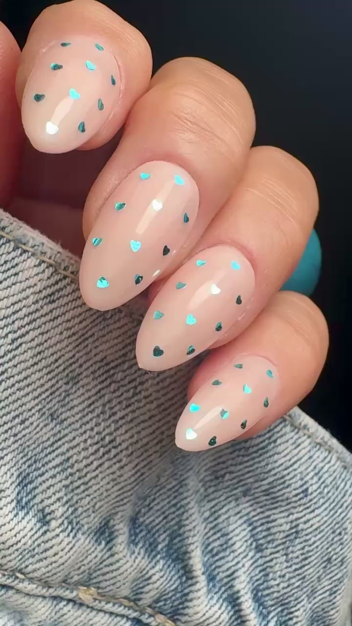 Video of nails with blue heart shaped glitter design on neutral background.