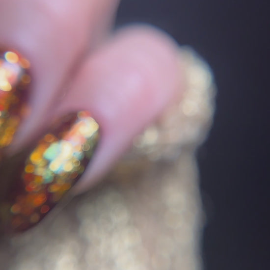 close up video of manicured hand with brown nail design with gold glitter detail on a dark background