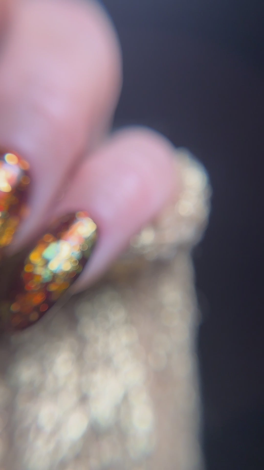 close up video of manicured hand with brown nail design with gold glitter detail on a dark background