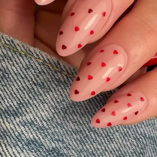 Video of manicured hand with red heart glitter design on neutral background.