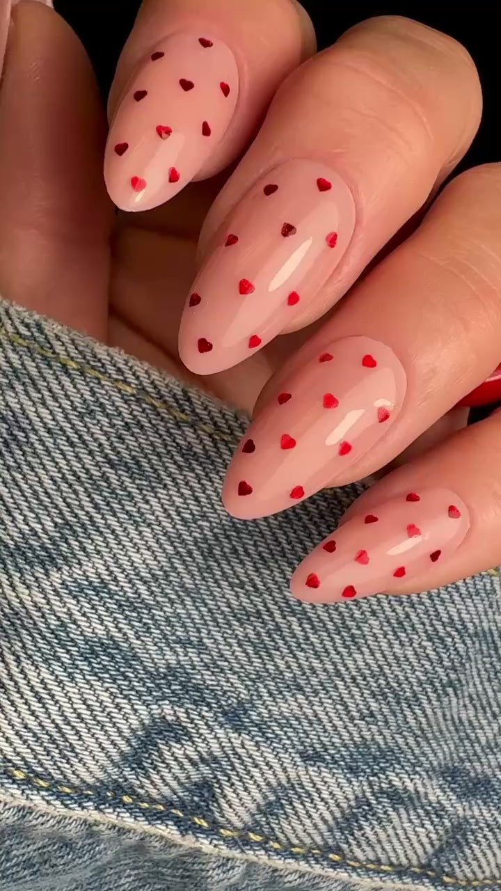 Video of manicured hand with red heart glitter design on neutral background.