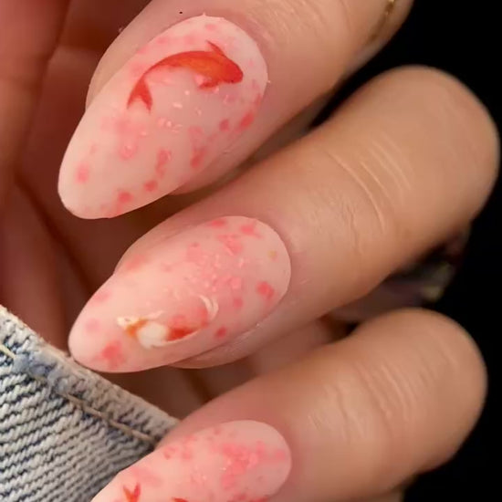 Video of manicured hand with orange speckled nails and koi fish design.