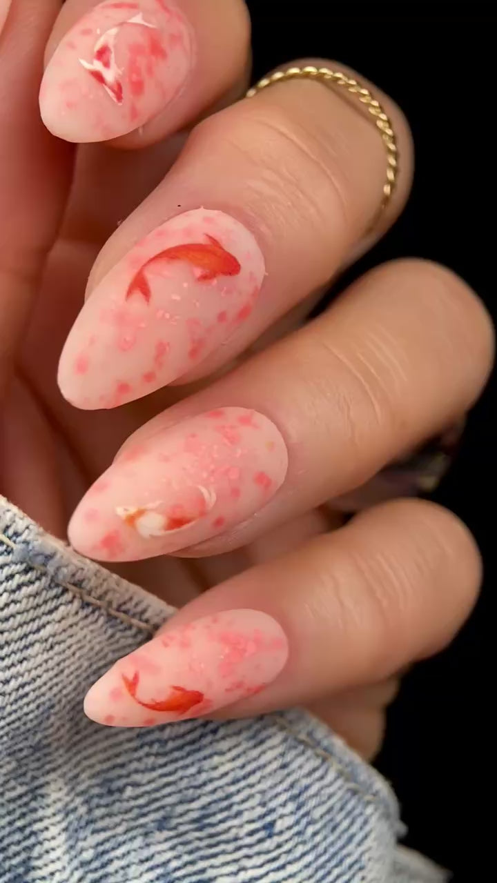 Video of manicured hand with orange speckled nails and koi fish design.