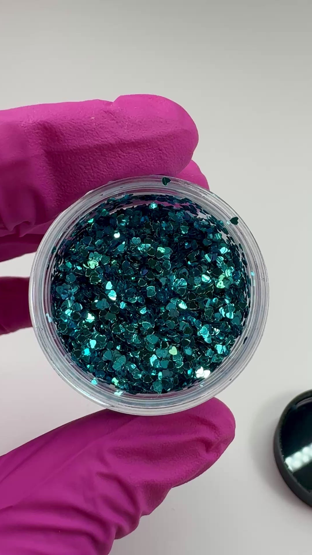 Video of gloved hand holding clear jar with textured glitter. 