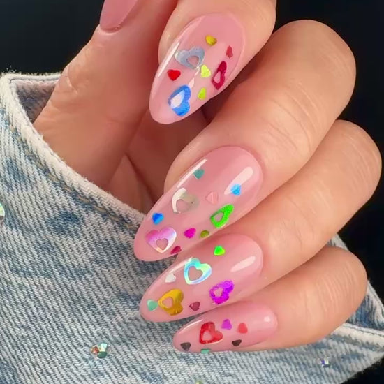 Video of manicured hand with colorful heart glitter on neutral background.