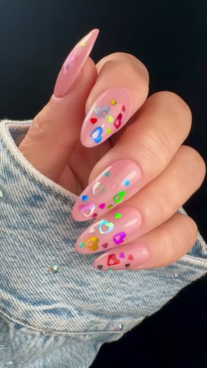 Video of manicured hand with colorful heart glitter on neutral background.