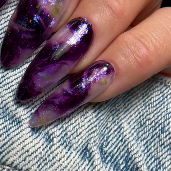 Video of manicured hand with purple iridescent marble nail design on denim background 