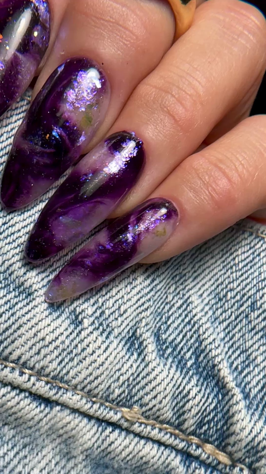 Video of manicured hand with purple iridescent marble nail design on denim background 