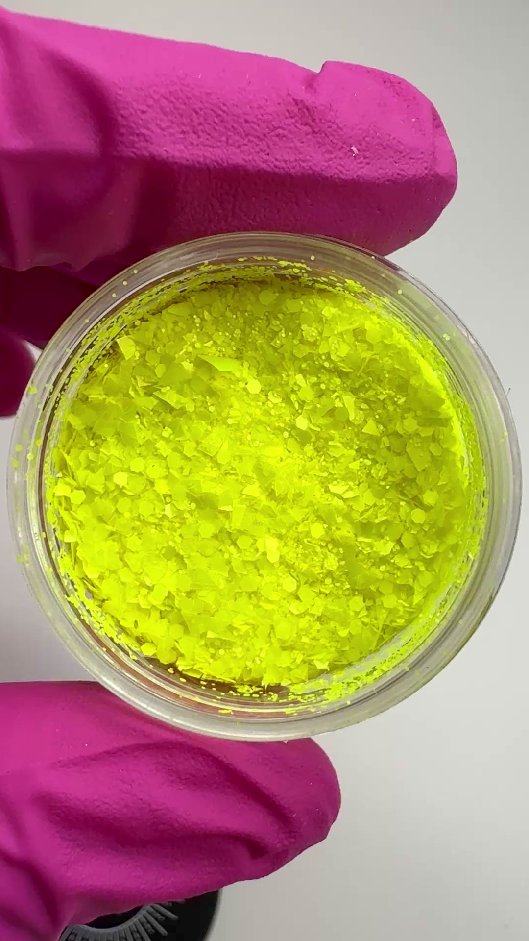 Video of hand in pink glove holding clear jar with textured glitter.