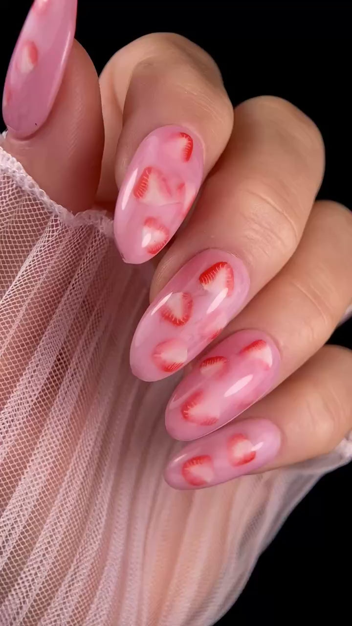 Video of pink nails with strawberry design with against black background. 