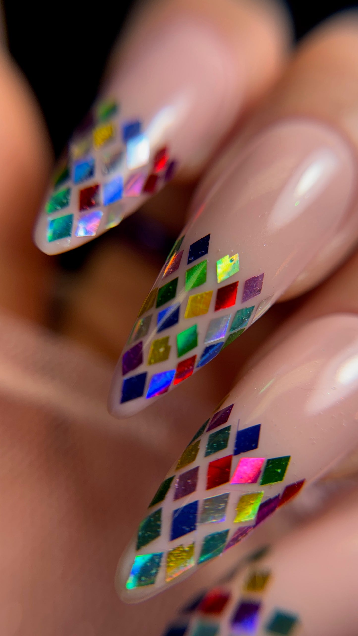 Close-up of a hand with multicolored diamond nail art on a blurred background