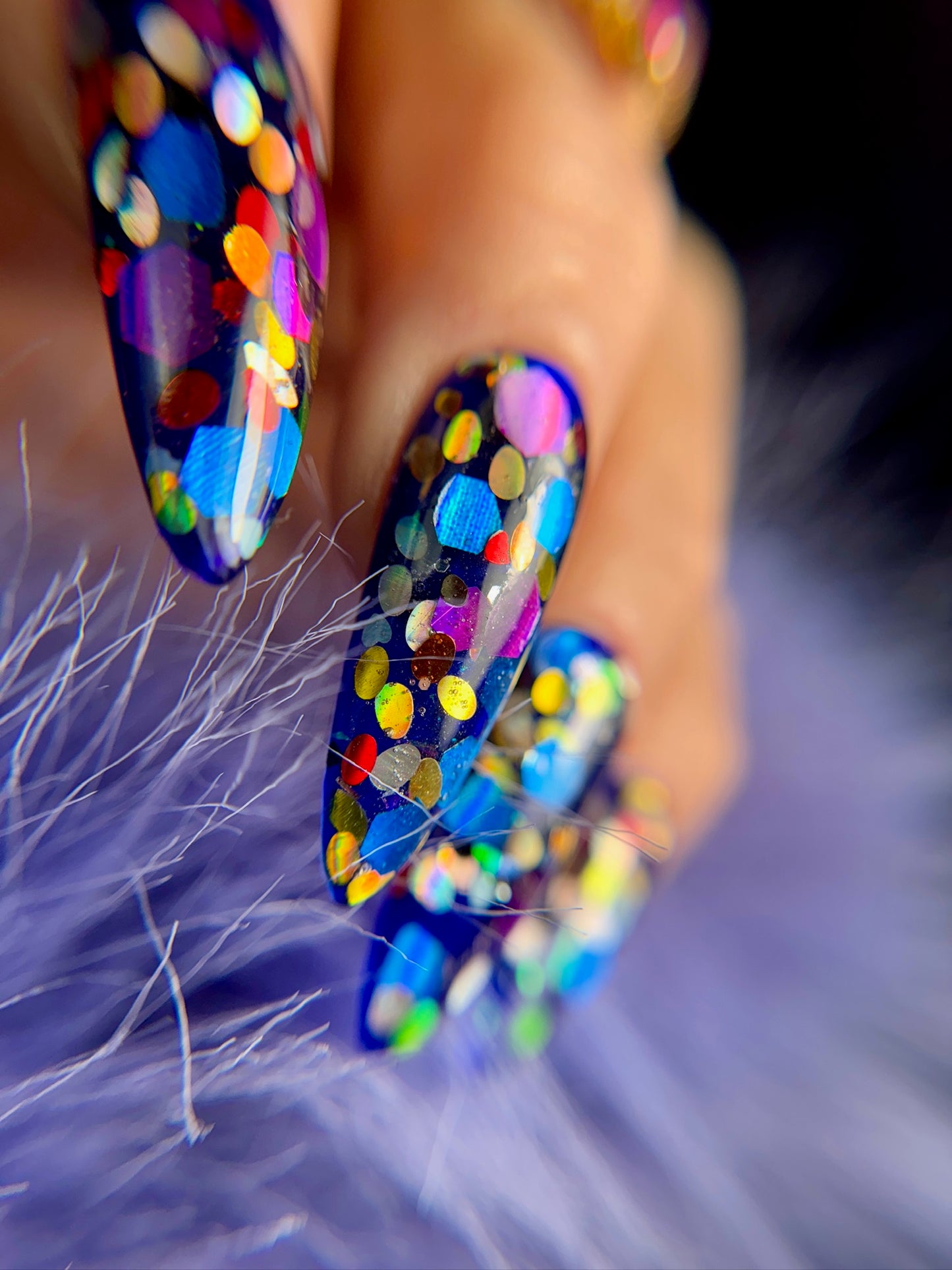Close-up of colorful glittery nail art on a fluffy purple background