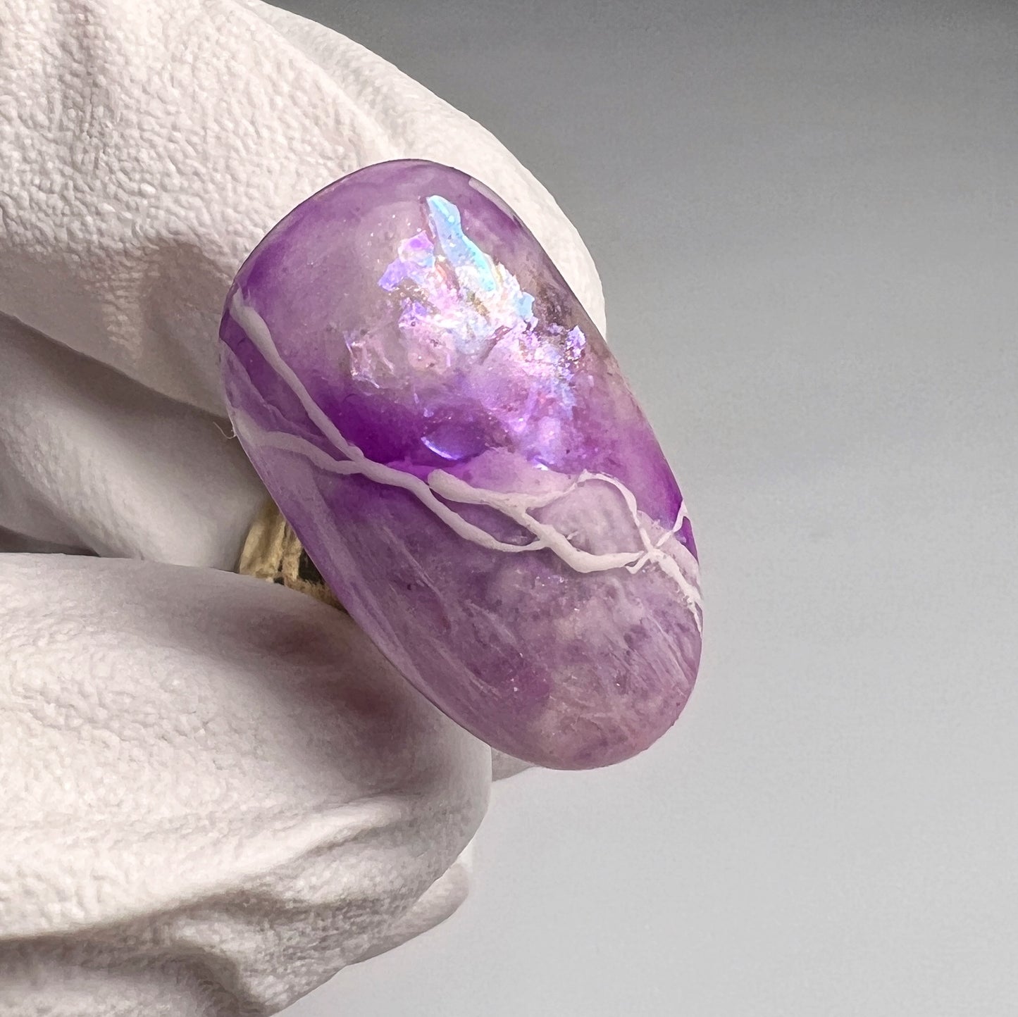 A close-up image of a purple quartz  nail art tip held between fingers, showcasing its translucent and sparkling purple hues.
