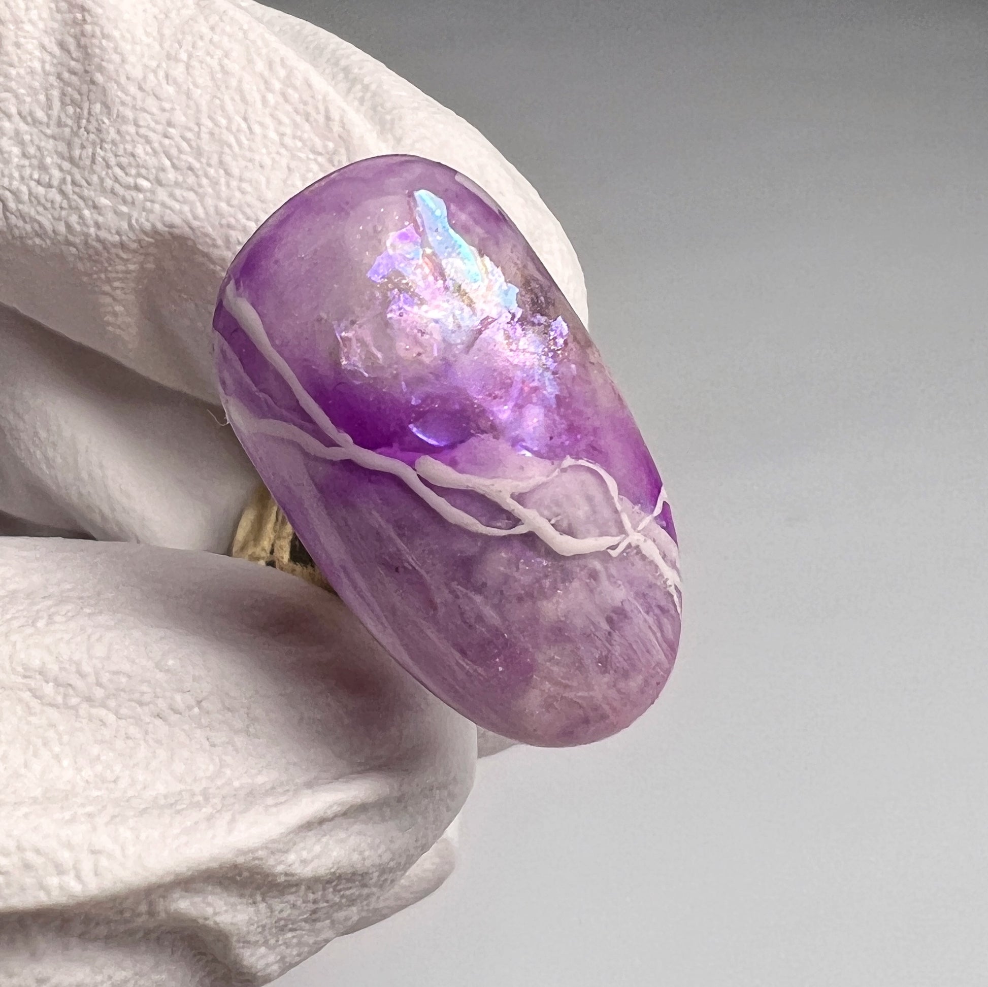 A close-up image of a purple quartz  nail art tip held between fingers, showcasing its translucent and sparkling purple hues.