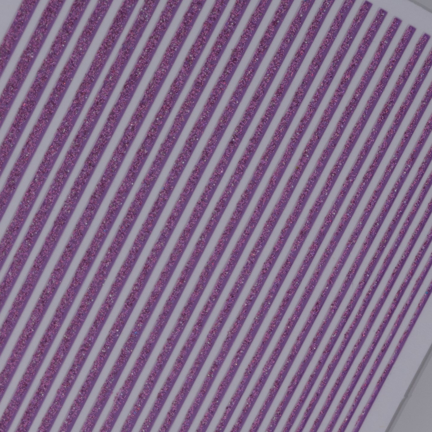 Close-up view of purple glitter line nail stickers on white background.