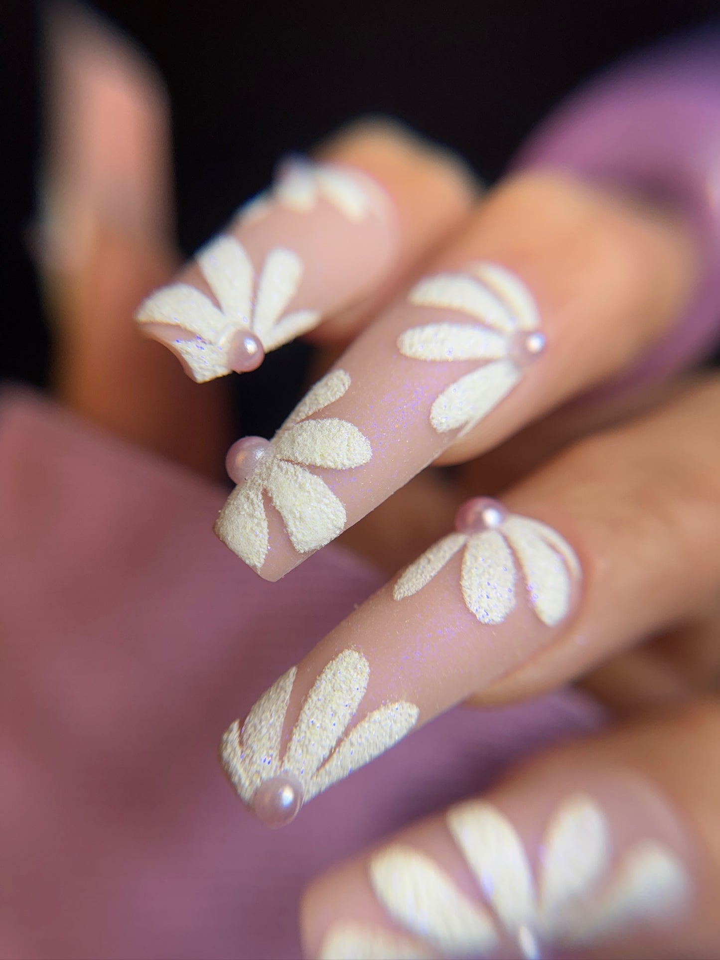 Nails with floral design and small pearls on a blurred background